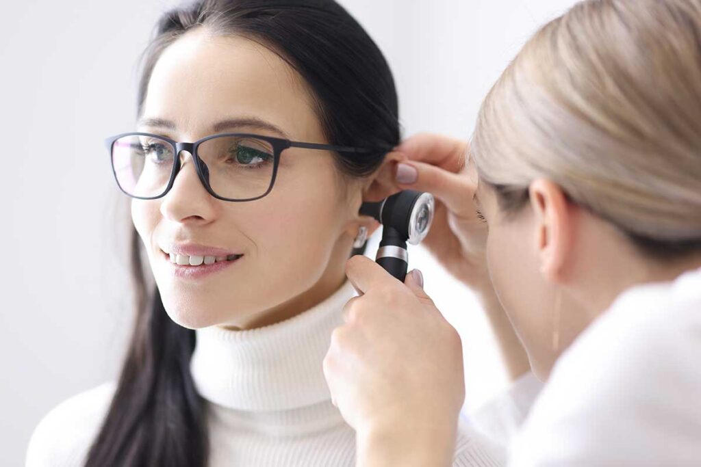 An adult male uses earmuffs while running a power tool in a residential backyard with green trees in the background.
