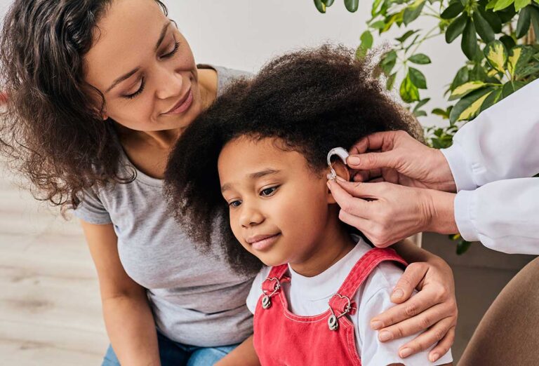 Parent and child wearing protective earmuffs while using hearing-safe practices outdoors.